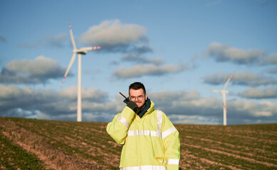 The wind park project manager speaks on VHF radio with massive wind generators in the background....