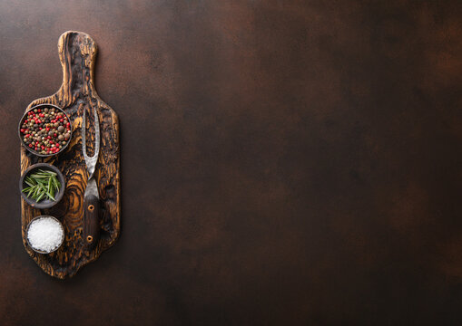 Chopping Board With Salt,pepper And Rosemary With Barbeque Steel Fork On Brown Kitchen Table Background.