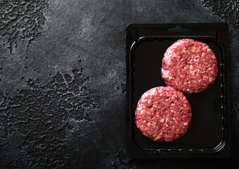 Raw minced beef burgers in plastick vacuum tray on black stone background.