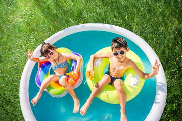 Children swim on inflatable circles in the blue water pool and drink orange juice. Top view, green grass lawn background.