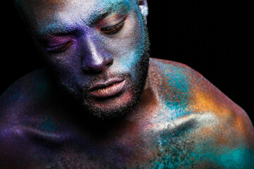 Black man in fantasy glitter makeup looking down on dark background in studio