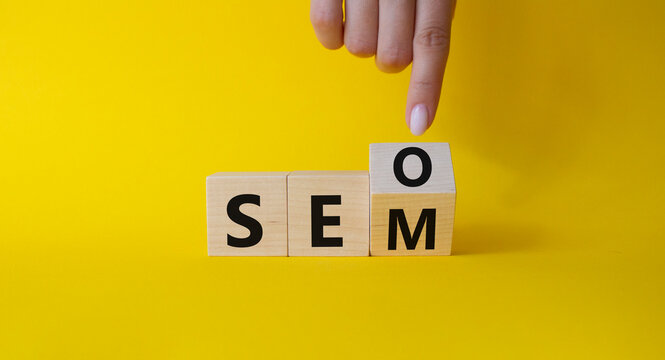 Seo and Sem symbol. Businessman hand points at turned wooden cubes with words Sem and Seo. Beautiful yellow background. Businessman hand. Business and Seo and Sem concept. Copy space