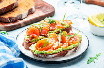 Avocado and salmon sandwich on rye bread with guacamole sauce, arugula and sesame seeds on plate, blue table background, top view
