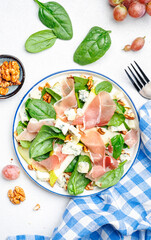 Summer pear salad with jamon, blue cheese, spinach and nuts on white table background, top view, copy space