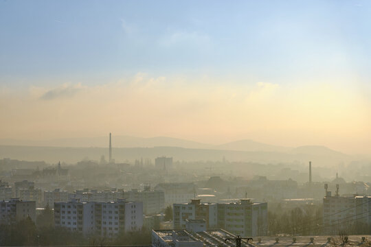 Smog air pollution over a small historic industrial town with mountains and hills in the background. Taken at sunrise with blue sky above the atmospheric inversion. 