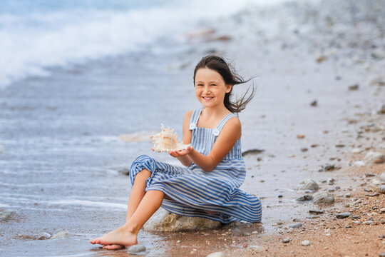 Little girl is playing with big white shell on the beach.