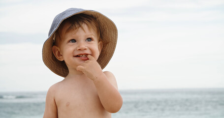 Copy space. Little baby standing on sandy beach, cute kid happily smiling and laughing - closeup shot. Portrait of a 1 years old boy on the beach in the summer. Childhood concept
