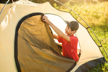 Teenage boy opens entrance to tourist tent. Active summer vacation in camp.