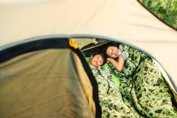 Two teenage children are sleeping in tent in sleeping bags. View from above.