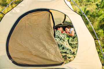 Happy family resting in tent in sleeping bags in summer.