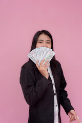 A young southeast asian woman elated to have a significant amount of cash on hand. Spending money concept. Isolated on a pink background.