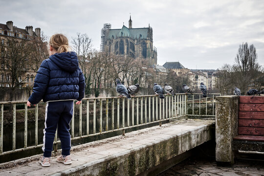 Petite fille embêtant des pigeons sur un pont à Metz