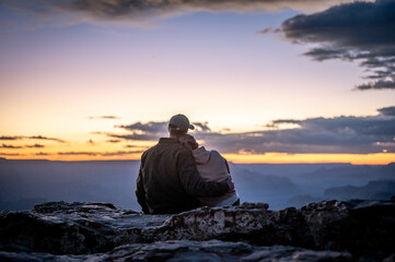 Wedding couple embracing sitting on the edge of the cliff of the grand canyon watching the sunset and sunset