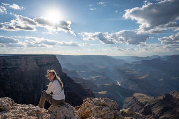 Portrait of a happy blonde young girl sitting on a rock at the edge of the precipice of the grand canyon