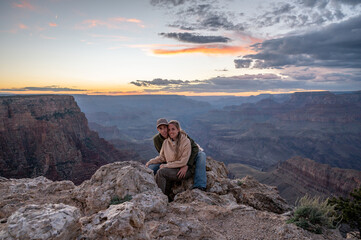 Young wedding couple hugging sitting on the rock of the precipice of the grand canyon at sunset