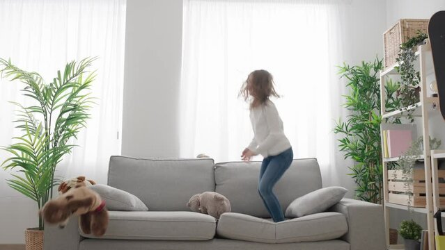 Kid throwing soft toys and jumping on sofa at home. Hyperactivity concept