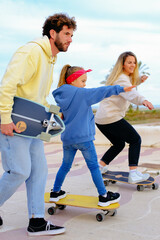 Happy family weekend. Mother father and doughter leisure and outdoor activity. riding on skateboards. Father holding and training his little child to ride a skateboard. Parenting vertical