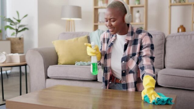 Music, dancing or black woman cleaning a table listening to radio on living room floor with a cloth at home. Headphones, cleaner or happy African maid working in a apartment with a liquid soap spray
