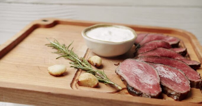  Sliced Beef Meat. Rare medium cooked beef with garlic and rosemary, white sauce and salt in a Woden plate. The salt falls on the meat. Restaurant Food. Rotating Plate on white background
