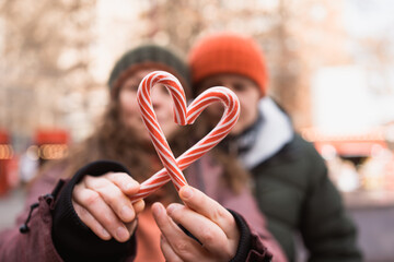 Couple in love making heart of two candies. Selective focus on lollipops, outdoors in winter
