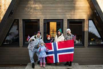 Fototapeta na wymiar Portrait of family with kids outside cabin house holding Norway flags. Scandinavian culture, norwegian people.
