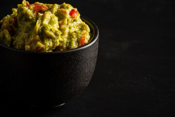 Close-up of black bowl with guacamole on black background, selective focus, horizontal, with copy space