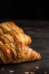 Close-up of croissants on board on dark wooden table with crumbs, selective focus, black background, vertical, with copy space