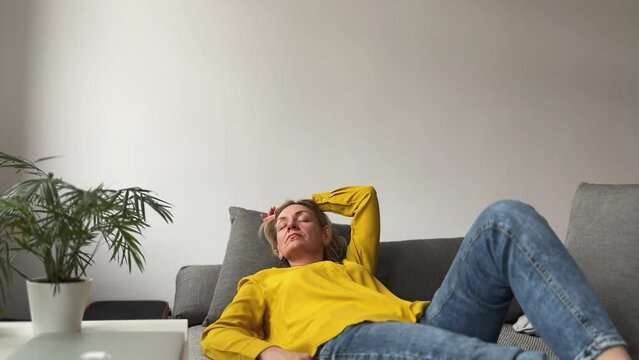 A middle-aged woman rests lying on the couch. She takes off her glasses for convenience. Concept of rest, migraine, menopause