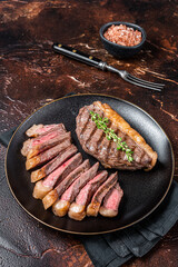 Sliced grilled medium rare Top sirloin beef steak on a plate. Dark background. Top view