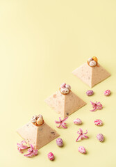 Traditional Easter cottage cheese dessert Paskha decorated with caramel and chocolate candy eggs and spring flowers on pastel yellow background. Modern minimalistic Easter background with copy space.