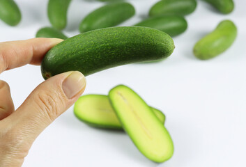 Close up of a hand holding mini avocado with a group of cocktail avocado on the back isolated on white. Specially cultivated exotic green vegan food for healthy living. Functional food or a superfood