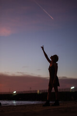 Fototapeta premium Girl Reaching for the Stars on a Beach at Sunset With a Colorful Sky in the Background.