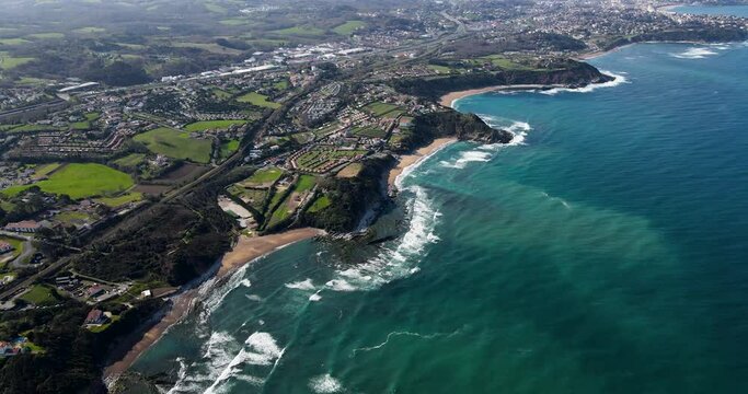 Aerial View of French Basque Country with many coastal homes and green landscapes with ocean waves breaking at the surf spots Parlamentia and Guethary close Biarritz, France