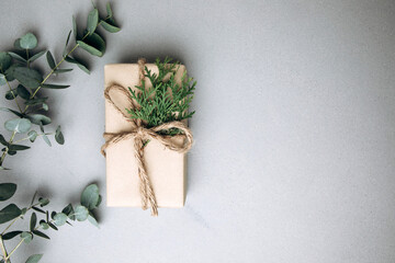 A gift wrapped in brown paper and decorated with a thuya branch on a gray concrete background with a eucalyptus branch. Flat lay