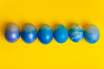 Blue dyed Easter eggs on bright yellow background from above.