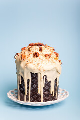 Vertical picture of tasty Easter cake decorated with white chocolate and pecan nuts on white round plate on blue background. Easter card.