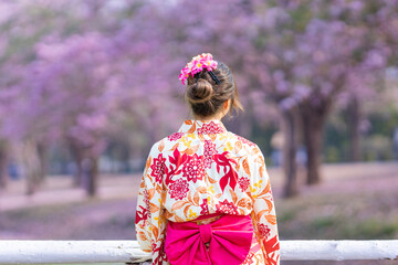 The back of Japanese woman in traditional kimono dress is looking at the view of sakura flower tree in the park at cherry blossom spring festival with copy space
