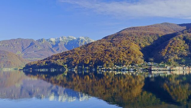 Snowcapped Mountain and Lake Lugano in Mirror Image a Sunny Day and Village Brusino Arsizio with Autumn Forest in Ticino, Switzerland.