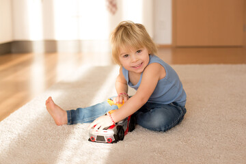 Cute blond toddler child, playing with big toy car