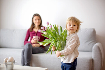 Beautiful blond boy, giving mother flowers and box with little gift for mothers day