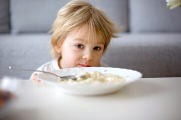 Cute toddler boy, eating pasta with white cheese at home