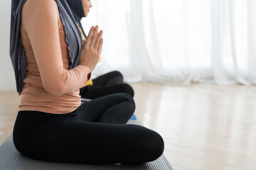 Two Asian young muslim woman doing meditate yoga asana on roll mat with eyes closed in home. Girl practicing doing yoga indoor