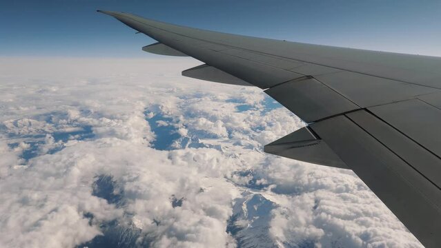 Flying on plane, view from window on wing. Flying over high snow capped mountains range and white clouds.