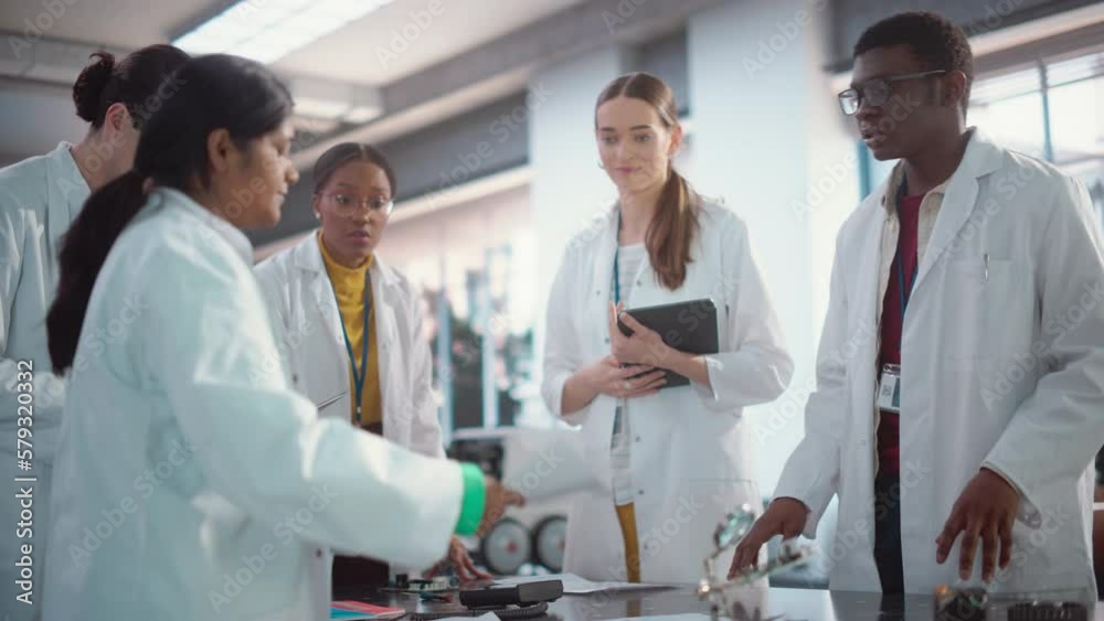 Poster Diverse Team of Industrial Robotics Specialists Gathered Around a Table to Discuss a Blueprint. Engineers In Lab Coats Using Laptop Computer and Tablet, Brainstorming Ideas For Electronic Components