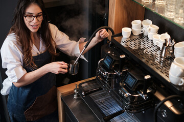 A happy barista is preparing coffee on a coffee machine in coffee shop.