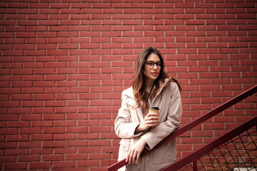 A casual woman standing outdoors on stairs and enjoying coffee to go.