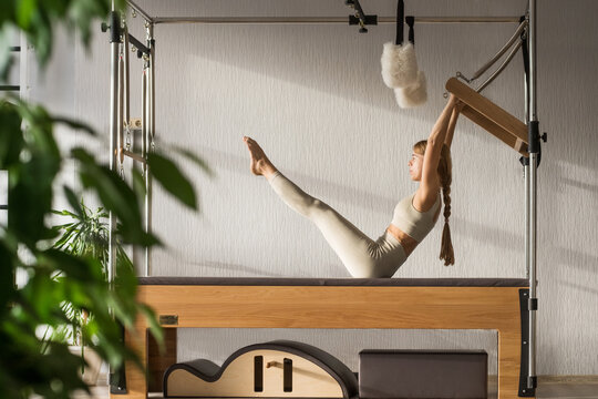 Pilates fitness trainer doing exercises on in pilates studio. Reformer pilates studio machine for fitness workouts in gym. Fit, healthy and strong authentical body. Fitness concept