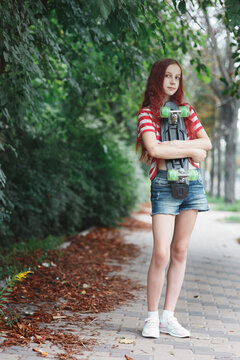 Young pretty girl teenager with long red hair standing with colorful penny board at city street or park alley in summer, urban outdoor lifestyle full length portrait of skateborder with copy space