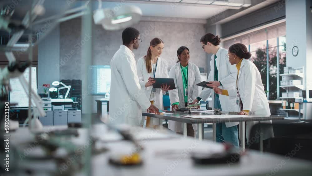 Poster Young Engineers Working in Company Facility Lab: Group of International Multiethnic Lab Specialists Gathering Around a Table to Discuss Blueprints and Components for a High-Tech Robotic Project