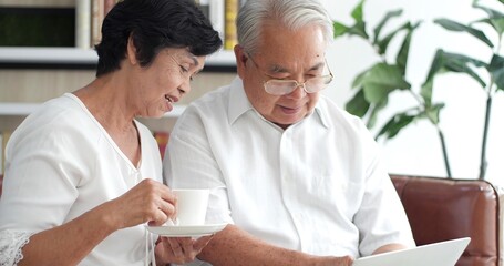 Happy Asian senior elderly couple using laptop talking together doing online shopping, senior...